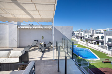 Fototapeta premium Modern rooftop terrace with lounge chairs overlooking shared swimming pool and residential buildings
