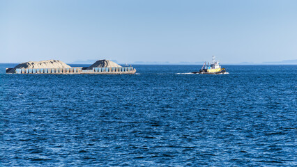 Tugboat  is pulling a barge of ore in open sea water