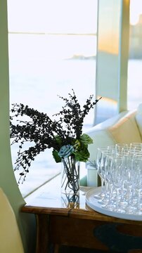 Elegant dark floral arrangement and rows of empty champagne flutes. A vertical interior view of a festive table setup with clear glasses and black decorative branches near a window.