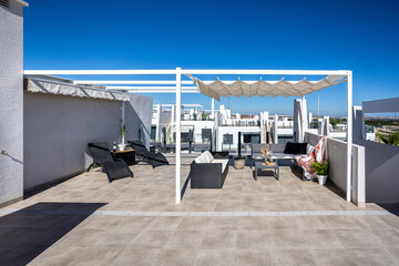 Fototapeta premium Spacious rooftop terrace with lounge chairs and shaded seating under clear blue sky