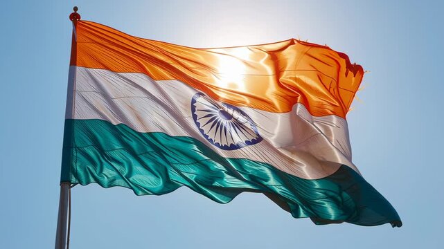 India's tricolor tiranga waving against a clear blue sky, sunlight illuminating saffron, white and green bands and the navy ashoka chakra, symbolizing unity and pride