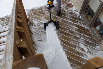 Partial view of an unidentifiable person shoveling snow off of a residential deck following a snow fall
