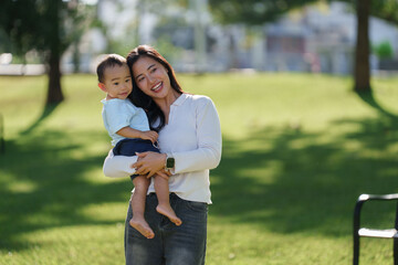 Happy asian mother holding baby boy in park