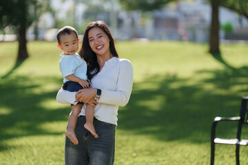 Young asian mother holding happy baby in park