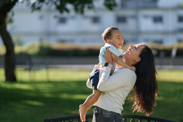 Mother lifting happy baby boy in park