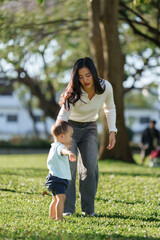 Mother teaching baby walking on green grass park