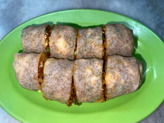 Sliced fried spring rolls (popia goreng) served on a green plate, traditional Asian street food