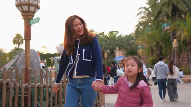 Asian mother and adorable daughter traveling together at theme park. 