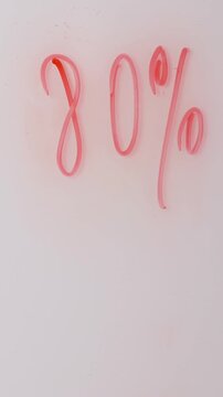 A hand is shown writing percentages on a white board using a pink marker. The text shows a significant savings on products during a special sale.