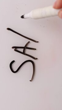 A hand uses a black marker to write the word sale on a white surface. The complete word is shown clearly. The promotion, discount, or deal can be seen.