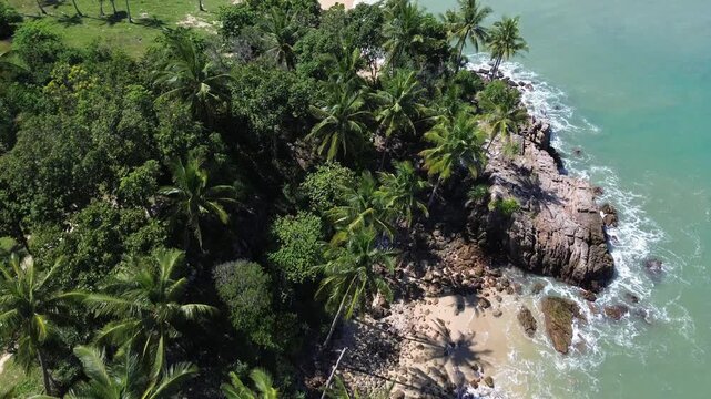 Aerial drone footage of a dense palm forest along a rocky shoreline on Koh Lanta island in Thailand featuring crystal clear turquoise water, small coves and lush tropical coastal scenery.
