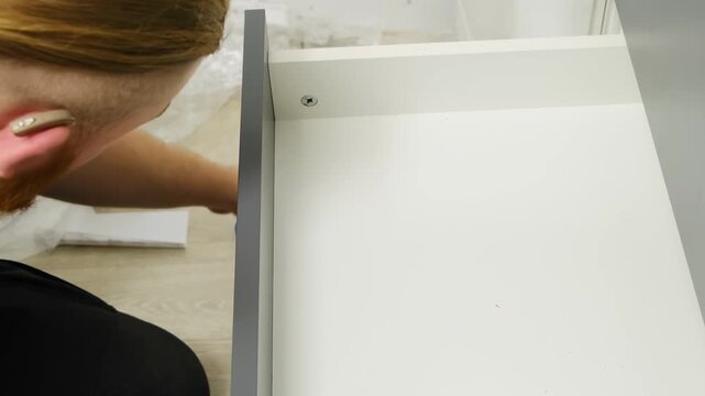 Specialist screws front of drawer in well-lit flat. Furniture assembly specialist forms complete construction and connects parts using special professional tools