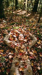 Smiling woman lying down covered in colorful autumn leaves on forest floor