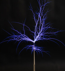 Streams of violet plasma discharge from the top of a Tesla coil in a high-voltage experiment