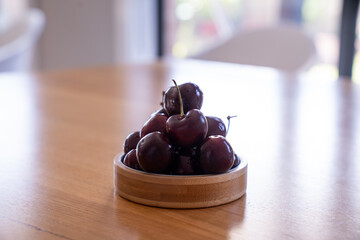 Fresh ripe dark cherries stacked in a small wooden bowl. Minimalist food photography with natural...