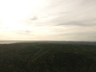 Fototapeta premium Aerial landscape of lush green rolling hills stretching to the horizon under a soft cloudy sky. Natural countryside scenery captured from drone, peaceful environment and untouched nature.