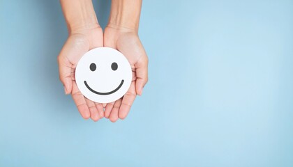 A person holds a white smiley face in their cupped hands against a light blue background, conveying a sense of mental health and positivity.