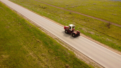 Fototapeta premium Aerial View of a Red Tractor Driving on a Paved Road Through Rural Fields
