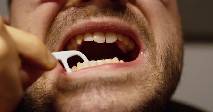 Close up shot of a man using a floss pick to clean between teeth, highlighting daily oral hygiene, self-care, and dental health routine.