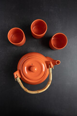 Minimalist flat lay of orange ceramic teapot and cups on dark gray background, vertical composition with copy space for text and design. Concept of cozy home tea moment and slow living