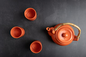 Top view of orange ceramic teapot and cups on dark gray background with ample copy space. Concept of modern tea ritual and minimalist lifestyle