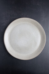 Beige ceramic plate photographed from above on a dark background, vertical format with copy space. Concept of simple dining and contemporary lifestyle