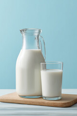 A jug and glass of milk on a wooden cutting board with blue background. Concept of farm dairy products, milk day