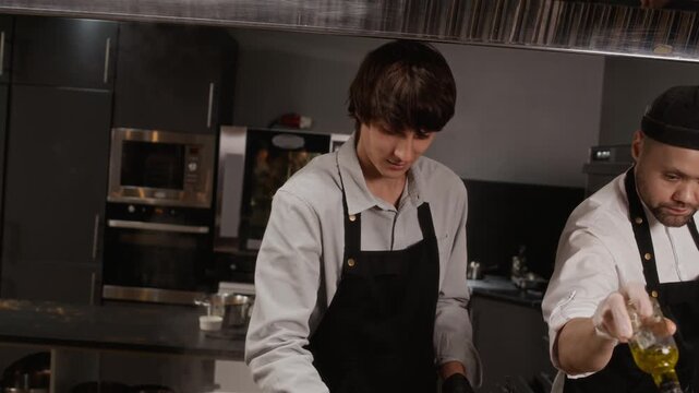 Handheld shot of male chef in apron and black nitrile gloves adding artisanal pasta to boiling water in stainless steel pot while cooking on restaurant kitchen stove
