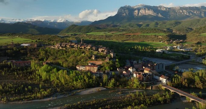 Aerial establishing shot of A&iacute;nsa, Huesca, Spain, framed by the towering limestone cliffs of Pe&ntilde;a Monta&ntilde;esa at the gates of the Pyrenees