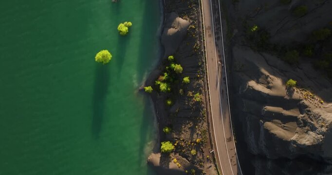 Vertical tracking shot of a bicycle transit through the derelict N-240 road and the abandoned sulfur springs of the Aragon region, featuring the turquoise waters of the Yesa basin.