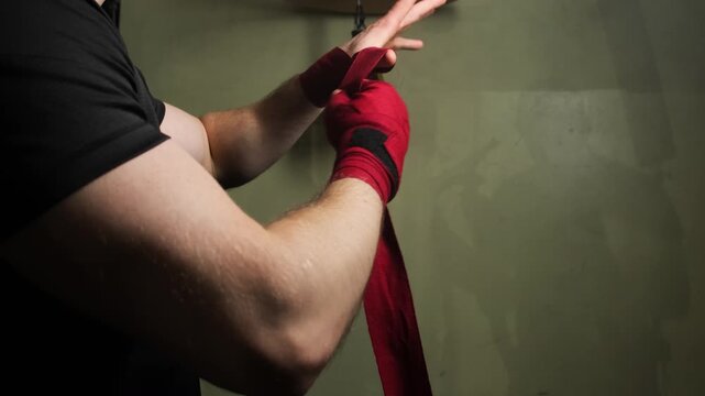 Athlete wraps bandage around arm against small speed bag Boxer prepares for warm-up and puts on protective fabric securing joints from displacement