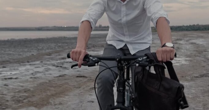 Straining man pedals forcefully across wet sand beach fighting resistant terrain showing thumbs-up. Bearded man maintains intense rhythm navigating difficult shoreline