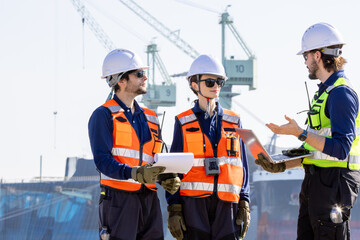 group of industrial engineers workers in a refinery - oil and gas processing equipment and machinery, engineers collaborate with a laptop, blueprint, and digital tablet at the oil storage tanks site.
