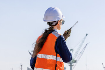 group of industrial engineers workers in a refinery - oil and gas processing equipment and machinery, engineers collaborate with a laptop, blueprint, and digital tablet at the oil storage tanks site.