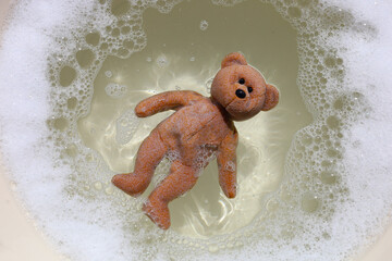 A brown teddy bear floating in soapy bubble water.