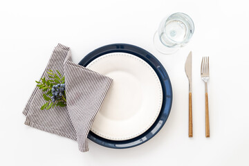 Festive table setting with empty plate and glasses, cutlery and napkin - green leaves decorated, flat lay. Top view