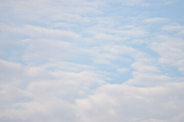 Peaceful view of soft white altocumulus clouds scattered across a bright, pale blue morning sky.