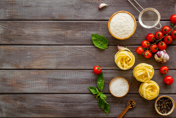 Fettuccine with ingredients for cooking pasta - tomatoes and basil with garlic - on a wooden background, top view. Flat lay