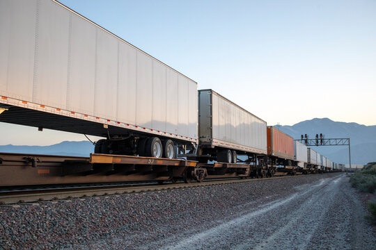 Long train of truck trailers on flatcars in baron landscape