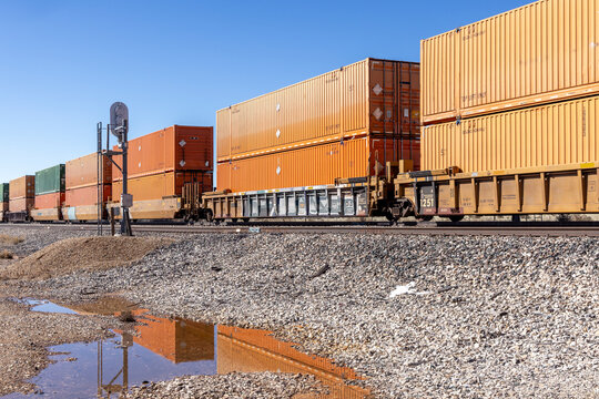 Orange shipping containers on a train reflected in puddle