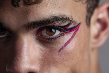 Fototapeta premium Young man wearing bold, vibrant eye makeup, featuring pink and black geometric lines, symbolizing self expression and gender fluidity