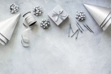Frame of festive party decoration with silver streamers and gift box and carnaval caps on gray stone background, top view
