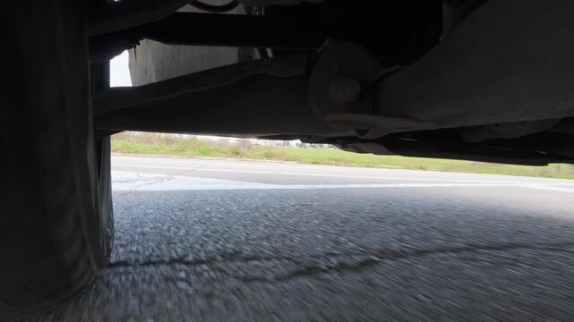 Low-angle POV drive video from an action camera mounted under a car, showing suspension and wheel movement with strong road motion. Automotive undercarriage view, speed, vehicle dynamics, travel and