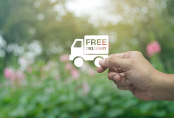 Hand holding free delivery truck flat icon in fingers over blur pink flower and tree in park, Business transportation service concept