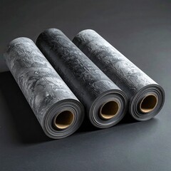 Three rolled-up dark gray mats.  A textured, gray-and-black pattern appears on the surface.  Smooth rolls rest on dark background