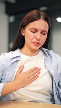 Woman at desk feels sudden sharp chest pain, breathing becomes difficult. Expresses distress, anxiety, and discomfort. Appears unwell and concerned about worsening symptoms.
