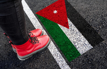 a woman with a boots standing on asphalt next to flag of Jordan and border
