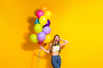 Happy young woman holding colorful balloons against yellow background, enjoying leisure time and...