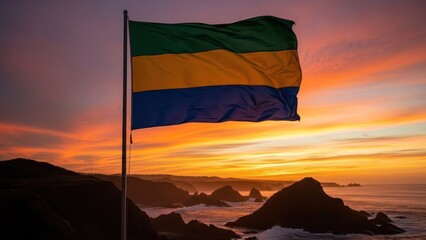 The flag of Gabon waves in the wind against a dramatic sunset over a coastal landscape