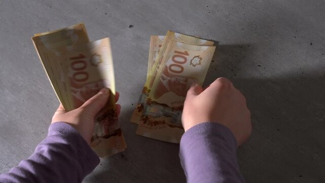 Close-up of a pair of hands holding a stack of Canadian $100 bills, then putting the money down to count each bill one by one.